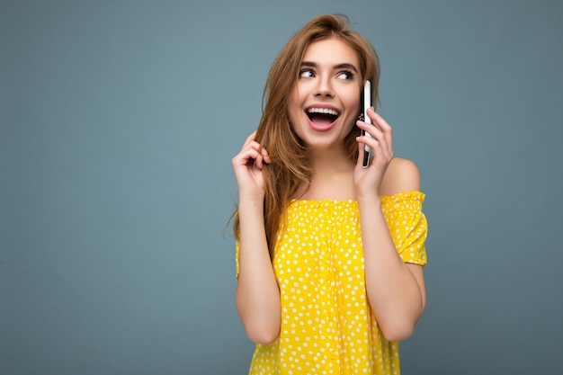 Aantrekkelijke positieve sexy glimlachende jonge blonde vrouw, gekleed in stijlvolle gele zomerjurk staande geïsoleerd