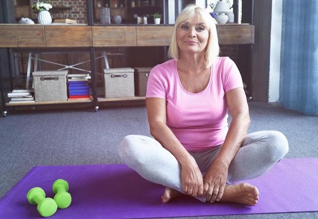 Aantrekkelijke rijpe vrouw die thuis op yogamat zit