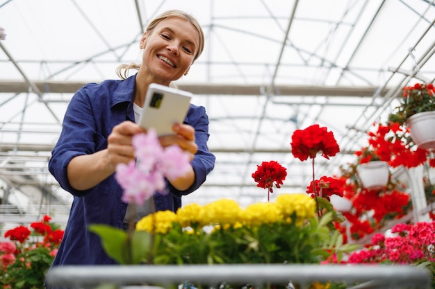 Aantrekkelijke rijpe vrouw in een kas die een foto maakt van bloemen op een smartphone