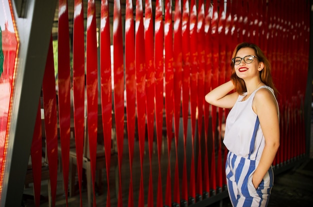 Aantrekkelijke roodharige vrouw in brillen poseren tegen rode achtergrond