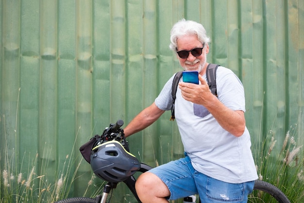 Aantrekkelijke senior man met helm en rugzak met behulp van mobiele telefoon terwijl u geniet van sportactiviteit met elektrische fiets in de buitenlucht duurzaam mobiliteitsconcept