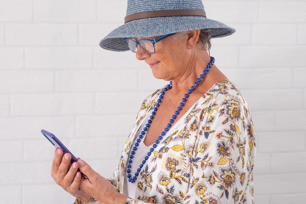 Aantrekkelijke senior vrouw met blauwe hoed en accessoires met mobiele telefoon glimlachend trendy dame met behulp van mobiele telefoon genieten van tech en social