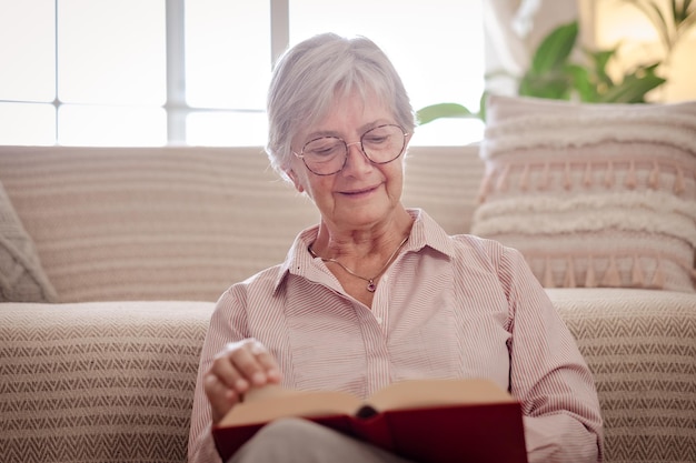 Aantrekkelijke senior vrouw zittend op de vloer thuis tijdens het lezen van een boek