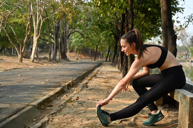 Aantrekkelijke sportieve vrouw die rust na een trainingssessie in het zomerpark bij zonsopgang Sport en gezond levensstijlconcept