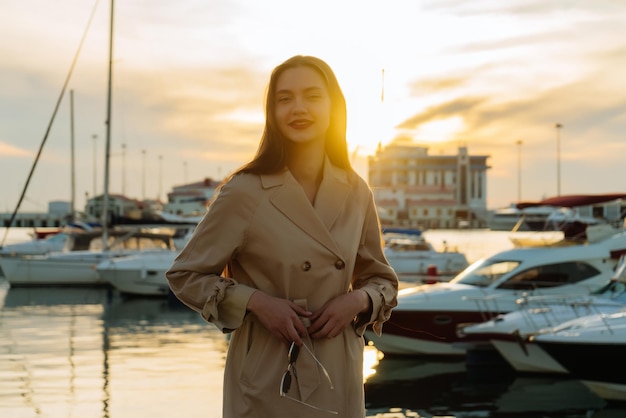 Aantrekkelijke stijlvolle jonge vrouw genieten van de warmte en zonsondergang, in de zeehaven