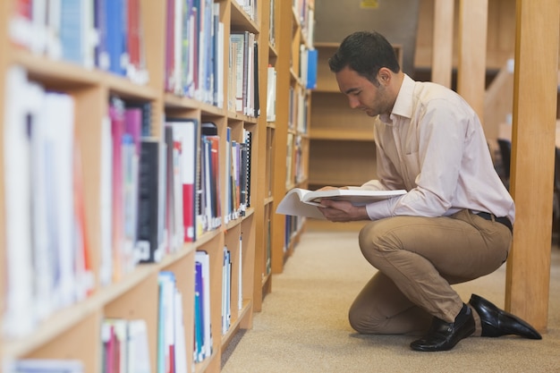 Aantrekkelijke toevallige mens die een boek in bibliotheek leest