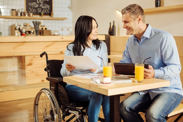 Aantrekkelijke uitbundige gehandicapte vrouw en een knappe gelukkig blonde man glimlachend en werk bespreken zittend in café