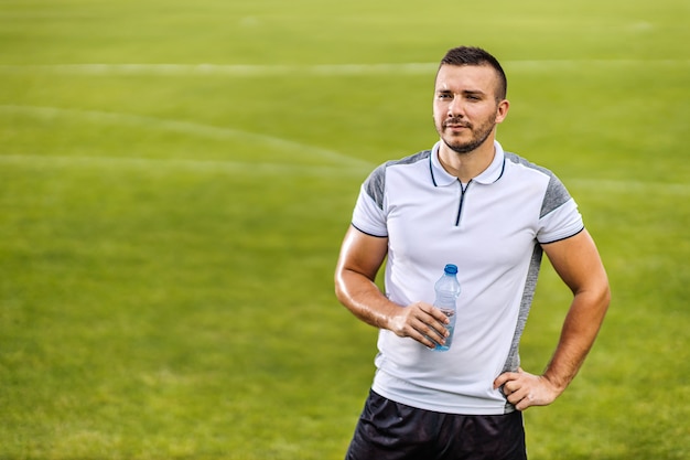 Aantrekkelijke voetballer in vorm staande op het veld en fles water te houden.