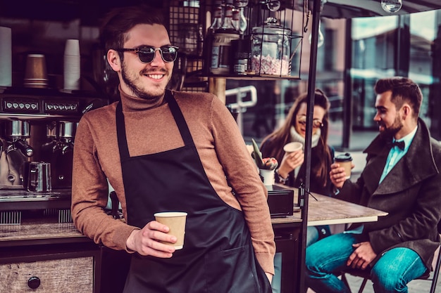 Aantrekkelijke vrolijke barista met zonnebril nam een koffiepauze in zijn eigen coffeeshop.