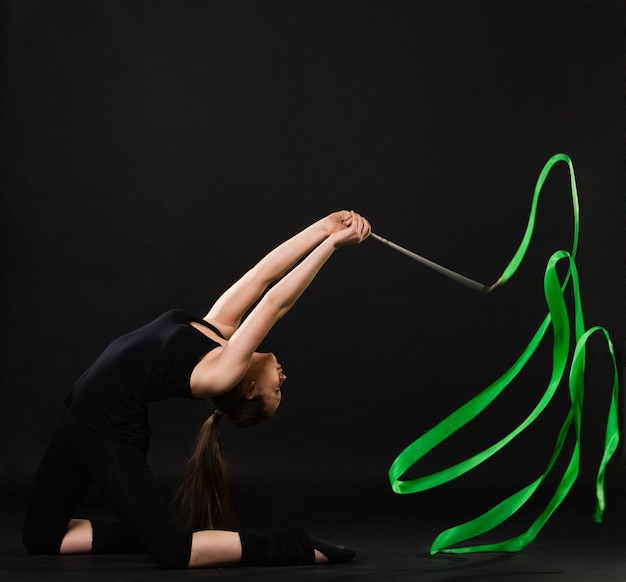 Aantrekkelijke vrouw dansen met groen lint tegen donkere achtergrond