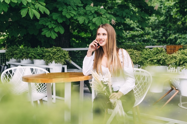 Aantrekkelijke vrouw die aan een tafel zit en naar de camera glimlacht en telefoon spreekt