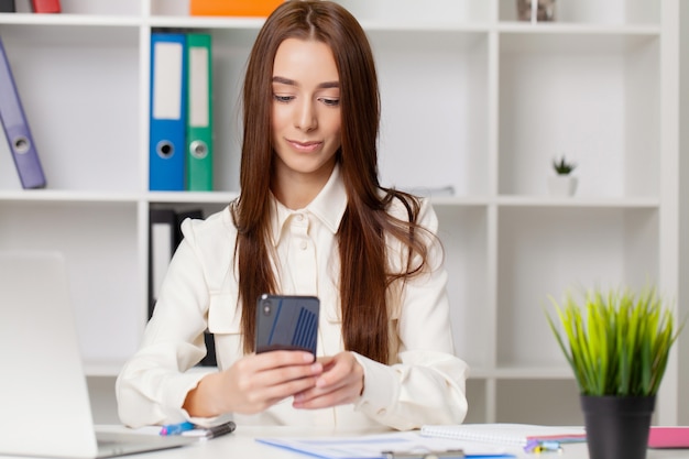 Aantrekkelijke vrouw die aan slimme telefoon in haar werkstation werkt.