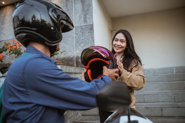 Aantrekkelijke vrouw die een helm ontvangt van een man die een motor berijdt langs de weg