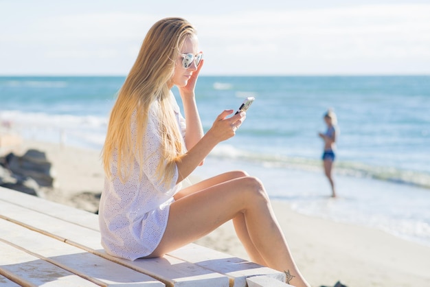 Aantrekkelijke vrouw die een telefoon op het strand gebruikt