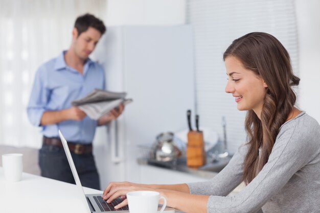 Aantrekkelijke vrouw die haar laptop in de keuken met behulp van