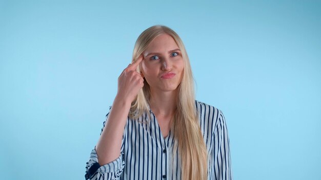 Aantrekkelijke vrouw die haar wijsvinger draait bij tempel op blauwe achtergrond ze kijkt naar camera met d...