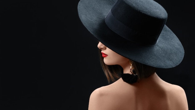 Aantrekkelijke vrouw die hoed het stellen op zwarte achtergrond draagt