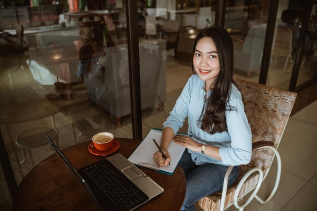 Aantrekkelijke vrouw die lacht tijdens het schrijven en werken met laptop in co-working space