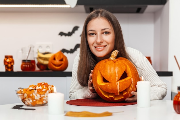 Aantrekkelijke vrouw die naar de camera kijkt en pompoen knuffelt voor halloween