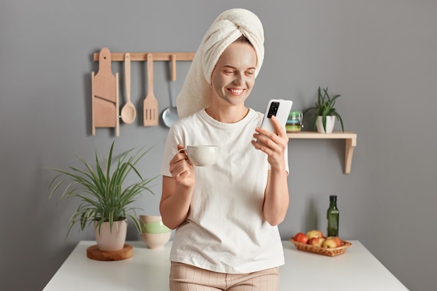 Aantrekkelijke vrouw die thuis ontspant en berichten leest op mobiele telefoon Gelukkig blank meisje gewikkeld in handdoek past collageenmasker toe na het douchen en het gebruik van mobiele telefoon Lichaamsverzorging schoonheid en wellness