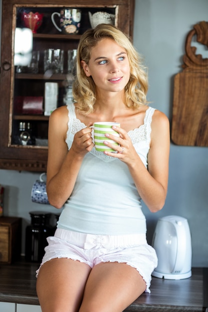 Aantrekkelijke vrouw die weg terwijl het hebben van koffie in keuken kijkt