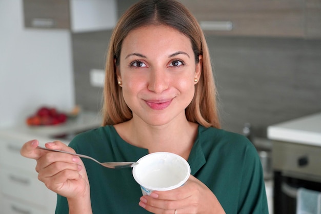 Aantrekkelijke vrouw houdt een kom Griekse yoghurt in haar hand en glimlacht naar de camera binnenshuis