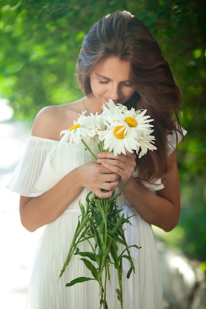 Aantrekkelijke vrouw in een witte zomerjurk met een boeket madeliefjes