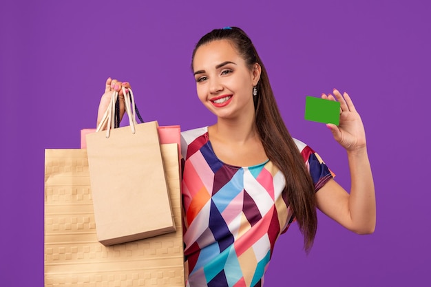 Aantrekkelijke vrouw in jurk met winkelpakketten en groene creditcard geïsoleerd over pu...