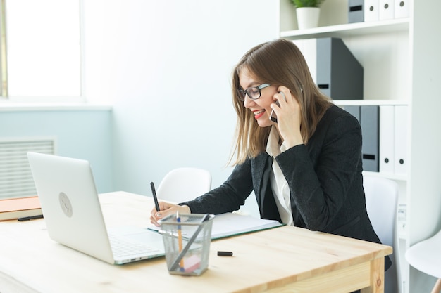 Aantrekkelijke vrouw in kantoor praten over de telefoon en notities maken