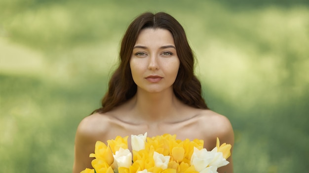 Aantrekkelijke vrouw in rode jurk met een boeket van lentebloemen tegen natuur bokeh groen