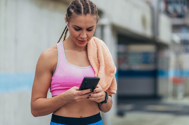 Aantrekkelijke vrouw in sportkleding die smartphone gebruikt na training en fitnessoefeningen buiten