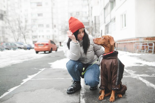 Aantrekkelijke vrouw in warme kleren, zittend op straat met een hond