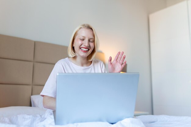 Aantrekkelijke vrouw in wit overhemd die laptop gebruikt en 's ochtends glimlacht videochat en freelance werken vanuit huis concept van mooie jonge vrouw met laptop in bed