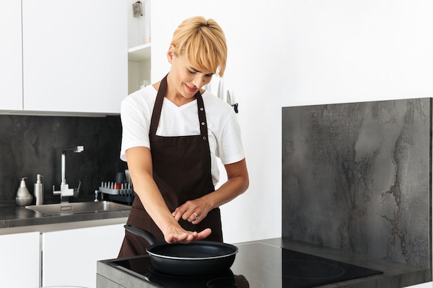 Aantrekkelijke vrouw koken met een koekenpan op een fornuis terwijl je in de keuken thuis staat