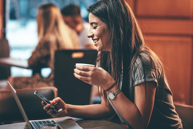 Aantrekkelijke vrouw leest goed nieuws van zakenpartners op laptop, zittend in café.