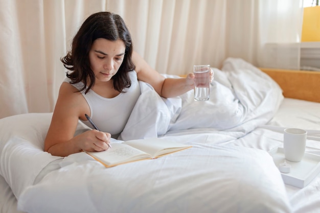 Aantrekkelijke vrouw liggend schrijven in dagboek en drinkwater