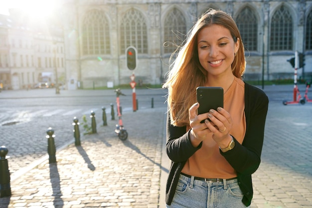 Aantrekkelijke vrouw lopen met behulp van mobiele telefoon op stedelijke achtergrond bij zonsondergang