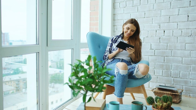 Aantrekkelijke vrouw met behulp van digitale tablet zittend in een stoel op balkon in loft modern appartement