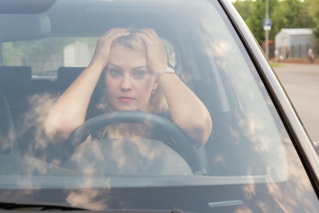 Aantrekkelijke vrouw met blond haar legde haar handen en hoofd op het stuur en kijkt droevig vooruit