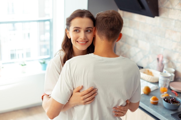 Aantrekkelijke vrouw met donkere ogen knuffelt echtgenoot in de keuken