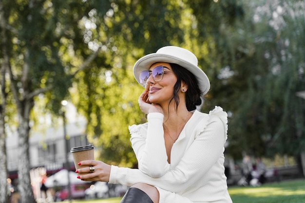 Aantrekkelijke vrouw met kopje koffie op het gras. Model weared witte officiële stijl geniet van koffie.