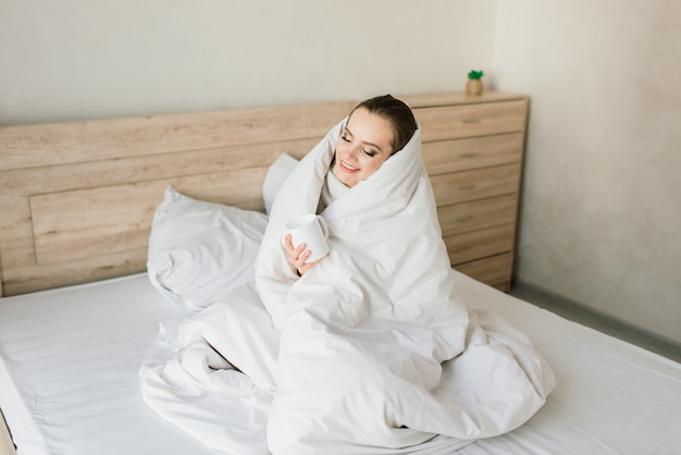 Aantrekkelijke vrouw met kopje koffie, smartphone en gebak in het bed