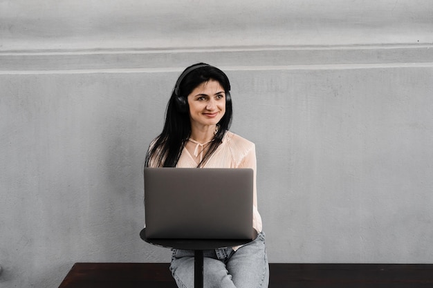 Aantrekkelijke vrouw met laptop en koptelefoon die online werkt aan werk op afstand en muziek luistert Schattig Georgisch meisje geniet van haar leven met muziek luisteren en chatten met vrienden