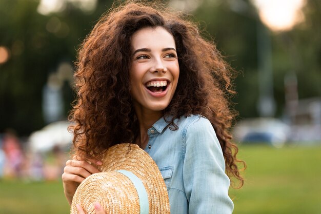 Aantrekkelijke vrouw met strooien hoed en lachen, tijdens het wandelen in groen park