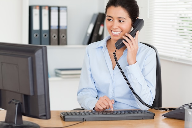 Aantrekkelijke vrouw op de telefoon tijdens het typen op een toetsenbord
