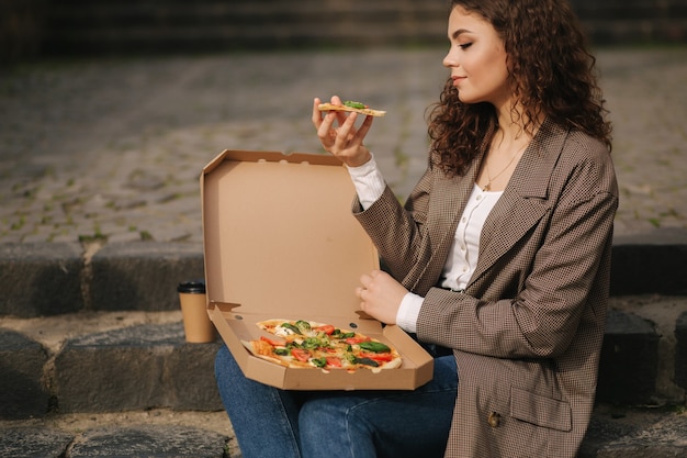 Aantrekkelijke vrouw open pizzadoos en veganistische pizza buiten eten