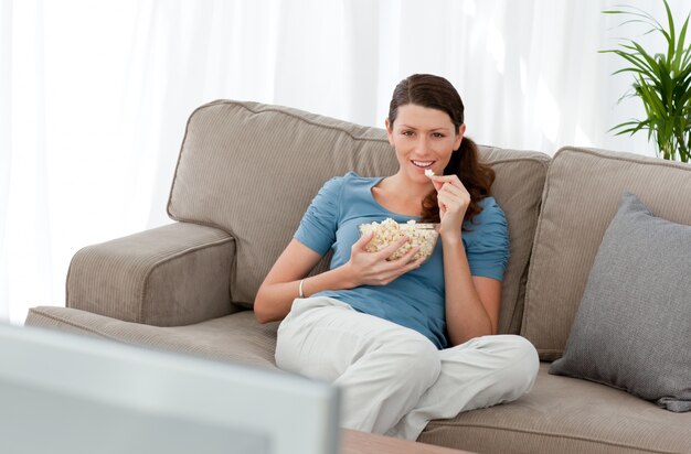 Aantrekkelijke vrouw televisiekijken en popcorn eten op de bank