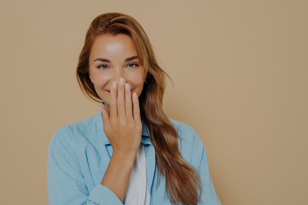 Aantrekkelijke vrouw verstopte mond terwijl ze plezier heeft op een beige achtergrond