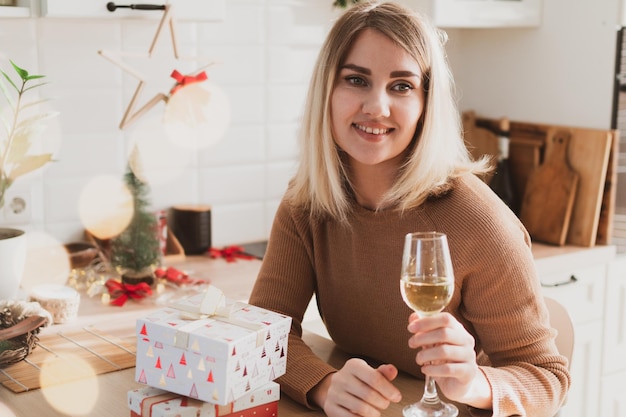 Aantrekkelijke vrouw zitten in de keuken met kerstcadeaus en glas champagne