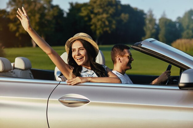 Aantrekkelijke vrouw zwaaiende hand met man rijden luxe cabriolet